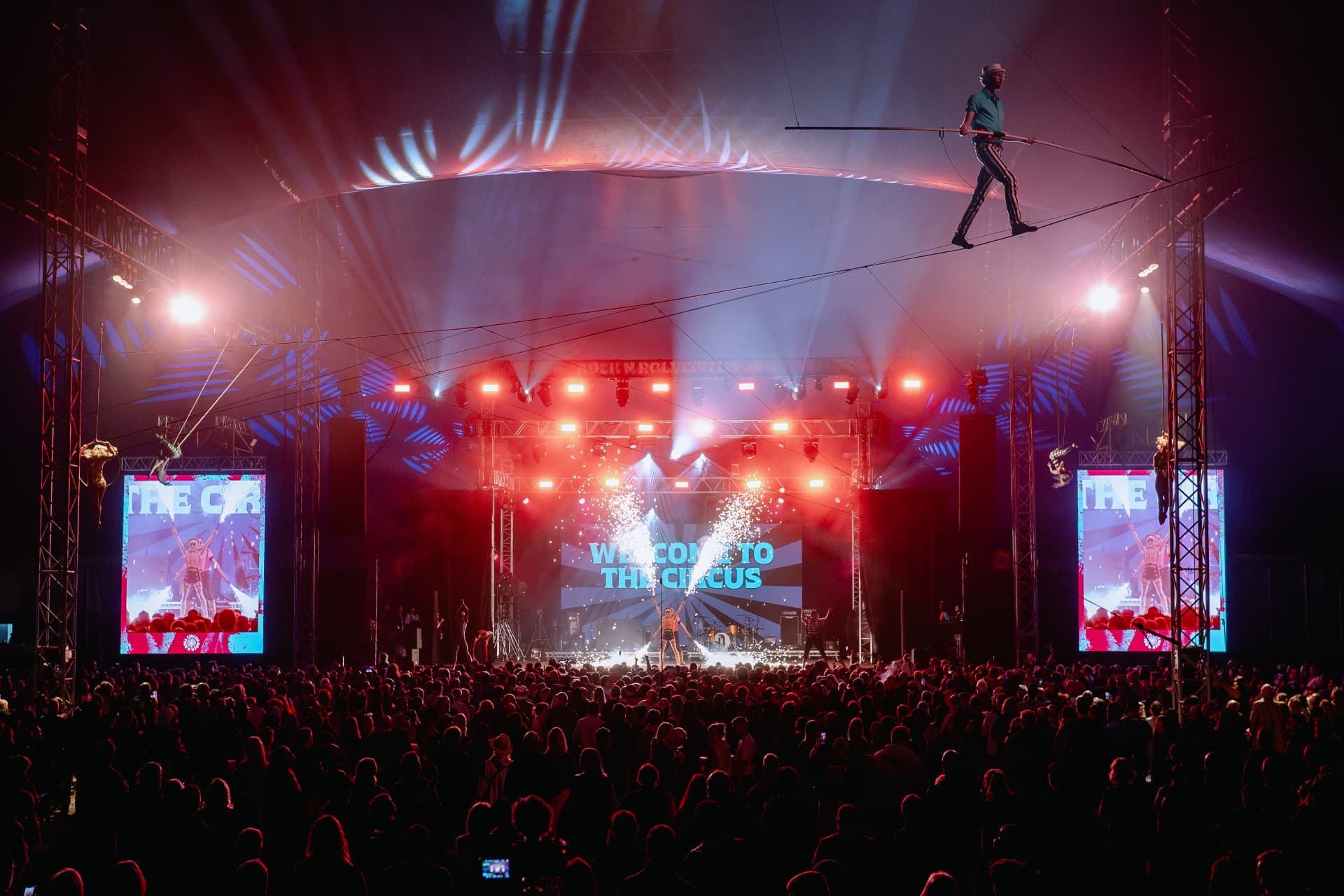 The Big Top lit in red and blue, with a high-wire act above a packed crowd