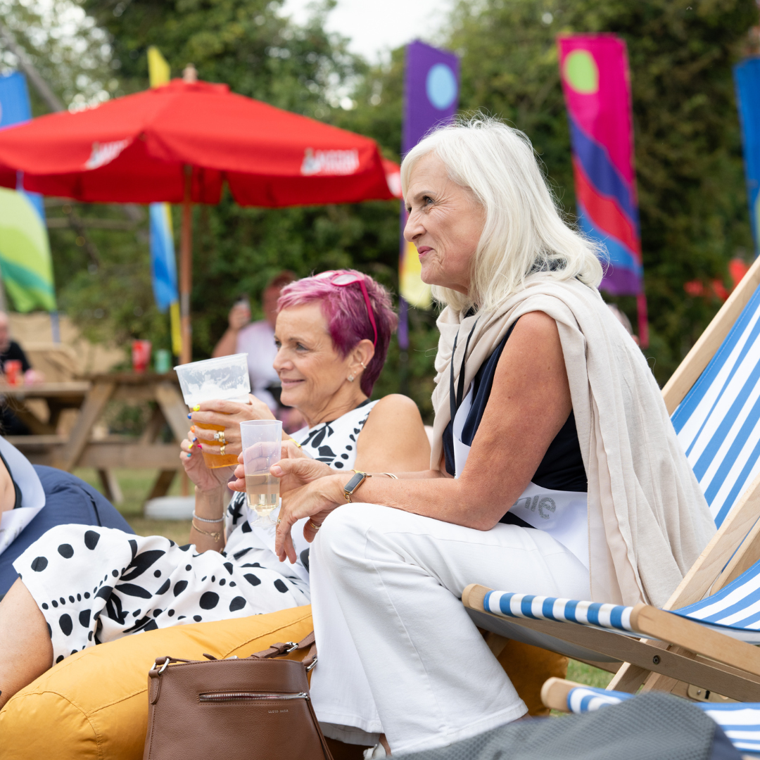 Two women enjoying drinks together in deckchairs on the festival lawn