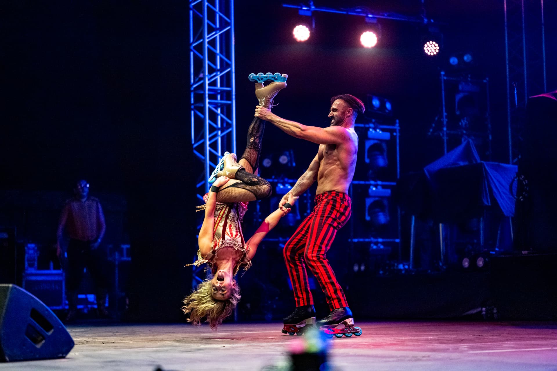 Two roller-skating circus performers lifting one another mid-air under stage lights