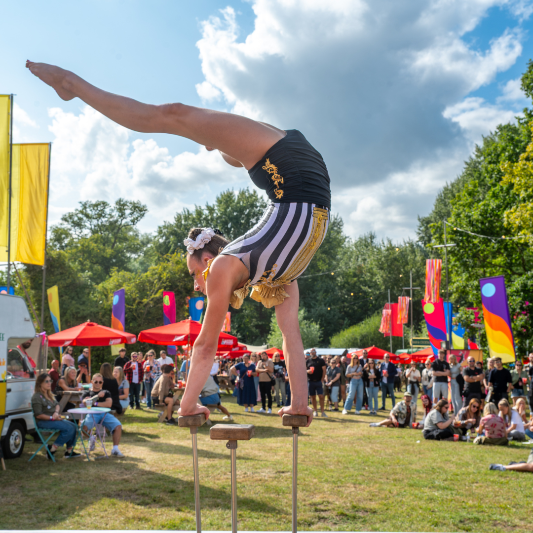 An acrobat balancing a handstand on wooden blocks in the circus arena while a crowd watches